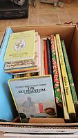 Photo of assorted children's books in box including The Sky Phantom, Beatrix Potter titles, Ladybird books