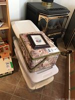 Photo of stacked white plastic containers with floral fabric sewing box on top near fireplace