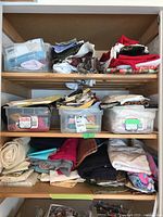 Three shelves filled with assorted folded fabric pieces and plastic bins containing more fabric pieces in a closet or shelving unit.