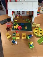Fold-out vintage Fisher Price schoolhouse with multiple colorful plastic figures, desks, chairs, and classroom accessories on a wooden table.