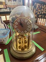 Full view of 12-inch tall Kern anniversary clock under glass dome, brass-tone base and rotating pendulum visible