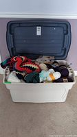 Wide view of filled plastic bin with knitting and crochet materials.