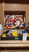 Box filled with mixed Lego bricks in various colors and shapes, some flat plates visible in foreground