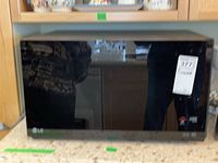 Front view of the black LG microwave with a glossy door showing reflections and LG logo.