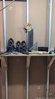 Wide shot showing nylon clamps, Craftsman saw, metal degree ruler, and mallets on wooden shelf against plywood wall