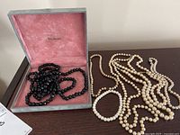 Showing black faceted beaded necklace inside Walters jewelry box with pink velvet lining, pearl necklaces and pearl bracelet laid out next to box.