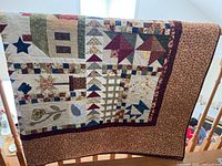Front of handmade quilt showing patchwork pattern with stars, birds, flowers, geometric blocks, and brown patterned border