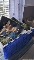 Partial view of a blue bin filled with quilting items including small patchwork art quilts with angel and star motifs.