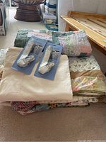 Stack of quilts with floral patterns, white flat sheet, and two packaged sheet straps on top