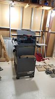 Full view of the Delta BT3000 jointer table saw stand in unfinished basement environment with lighting and shelving visible.