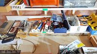 Shelf with hand saw, caulking tubes, caulking applicator, red and white tubes, hand tools and storage containers