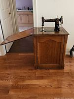 Side view of the closed oak cabinet with sewing machine mounted on top and hinged workspace extension open.