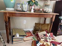 Front view of wood console table with some decorative items on top and stacks of books underneath. Shows turned legs and wood grain on table surface.