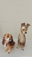 Two ceramic figurines of Disney dogs Lady and Tramp, shown from frontal view on white surface against plain background.