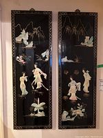 Full view of both Asian art panels side by side showing figure and nature designs in mother-of-pearl on black lacquer background.