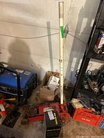 Red hydraulic car jack with a white handle, displayed leaning against a wall in a garage. The jack shows signs of usage and wear, including some rust and dirt on the lifting platform.