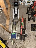 Three car jacks placed on garage floor. White floor jack with maxsold label, blue and silver Honda jack, red and black hydraulic jack.