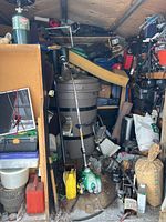 Photo of shed contents showing water barrel, green gas trimmer, motors, tools, and stacked items