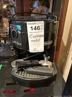 Front view of black DeLonghi Caffe Italia espresso maker with portafilter and coffee scoop placed on drip tray.