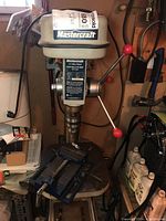 Front view of the Mastercraft drill press with visible head, spindle, and vise on the table.