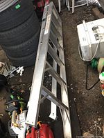 Photo showing aluminum extension ladder laid flat on the ground in a shed environment, close to stacked tires and other equipment.