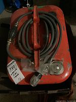 Top view of orange marine gas tank showing handle, wrapped fuel hose with manual pump bulb, metal filling cap, and paint wear.