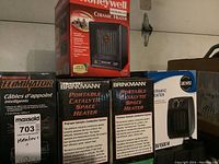 Several boxed space heaters and an electric winch arranged on garage floor and shelf, clear brand names and product model info visible on boxes.
