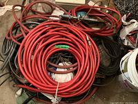 Photo showing several red coiled hoses laid on the ground with other items partially visible.