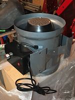 Metal inline fan with mounted black control box, power cord coiled in front.