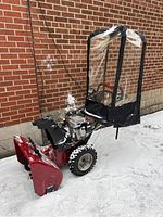 Side view showing red powder-coated steel auger housing, large treaded tires and attached clear vinyl cab