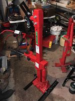 Strut coil spring compressor standing upright in a garage setting among other tools and equipment.