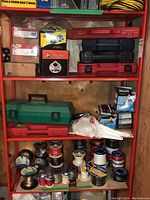 Red metal shelving with tool cases, wire spools, halogen bulbs, and supplies.