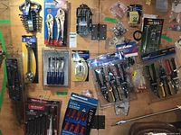 Full overview of all tools laid flat on wood surface showing a variety of hand tools including wrenches, pliers, snips, screwdrivers, hardware fittings, and accessories.
