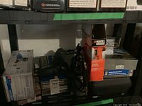 View of tools and various boxed items stacked on metal shelving, including angle grinder and black handheld power tool.