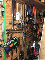 View showing various hand tools hung on plywood including multiple claw hammers with wooden handles, adjustable wrenches of different sizes, a 21-piece hex key set in original packaging, pliers and grips.