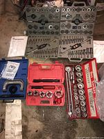 Overview of multiple socket sets, tap and die sets, and boxed tool sets on floor showing cases in red, gray, and blue colors and assorted tools within.