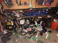 Wide view of mixed tools, hardware, electric motor, automotive parts all arranged on garage floor and shelving