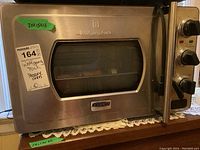 Front view of a stainless steel Wolfgang Puck Pressure Oven showing the door with window, large handle, and a label indicating measurements 20x13x13.