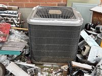 Front view of gray metal condenser unit among debris