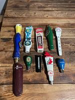 Photo showing all 10 beer tap handles on a wooden table with varying shapes and colors.