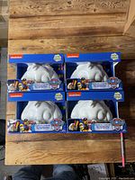 Four Paw Patrol Glow Buddies in original packaging on wood floor, arranged in two rows of two.