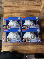 Four boxed Paw Patrol Glow Buddy color-and-glow kits arranged in a 2x2 grid on wood surface.