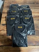 Seven black men's collared dress shirts individually packaged, laid out on a wood table