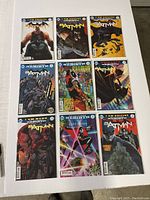 Nine Batman comic books arranged in a 3x3 grid on a white surface showing varied cover art including Batman in different poses and scenes.