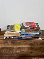 Two stacks of assorted vintage books and magazines on a wooden surface against a white wall.