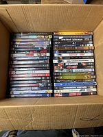 Top-down photo showing a box filled with two rows of DVDs stacked vertically with visible titles and artwork on spines.