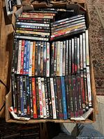 Top view photo of a large box filled with DVDs arranged in rows, showing titles from various genres, mainly movies and TV series.