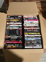 Top view of a cardboard box full of DVD cases arranged in two columns showing a variety of movie titles.