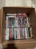 Top-down view inside the first box of DVDs showing a diverse collection of movie DVD cases arranged standing upright and stacked horizontally.