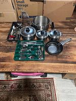 Overview of kitchen items including pots, frying pans, cutlery tray, and utensils on wooden table